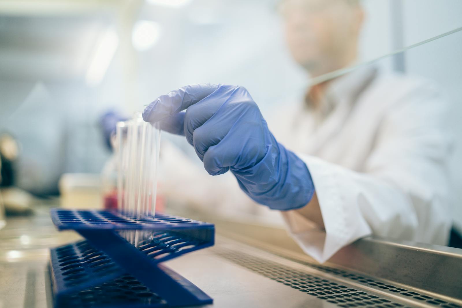 Close-up of a scientist wearing gloves and handling test tubes in a laboratory environment.